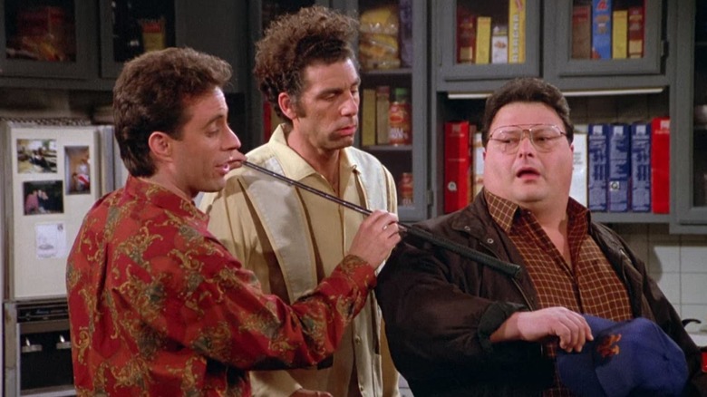 Jerry indicating Newman's wrist with a golf club while Kramer looks on