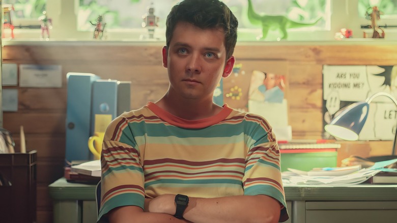 Asa Butterfield sitting with his arms folded