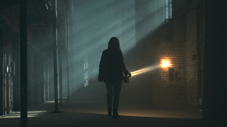 A woman walks in a dark building with a flashlight in 