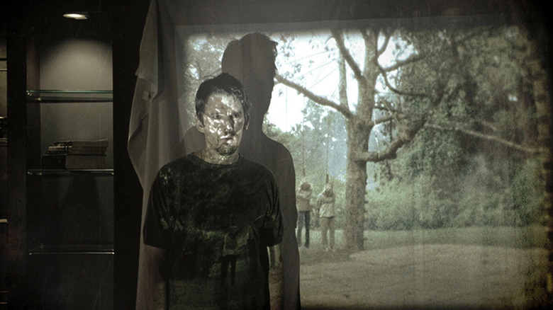 Ellison standing in front of a projector screen displaying a home video