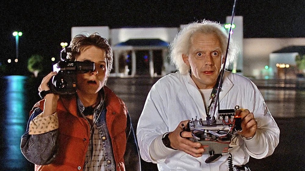 Michael J Fox as Marty McFly holds a very '80s video recorder up to his eye while Christopher Lloyd as Doc Brown holds a remote control to the DeLorean in Back to the Future