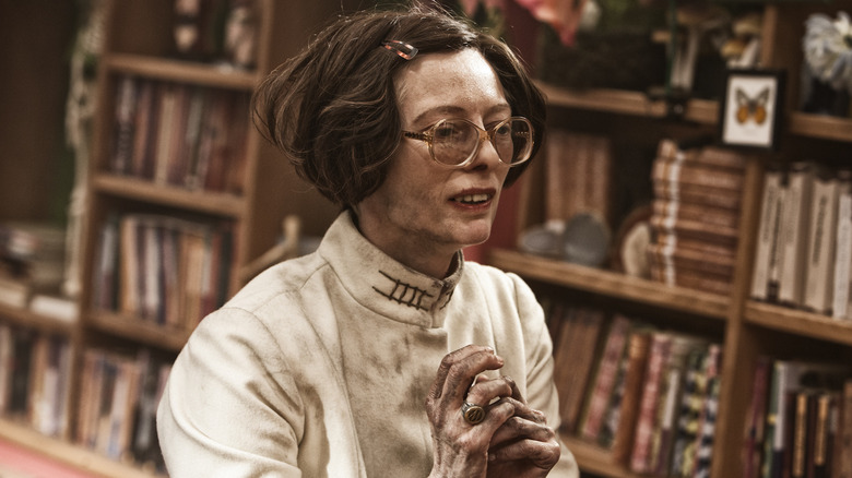 Minister Mason standing with hands clasped in front of bookshelves
