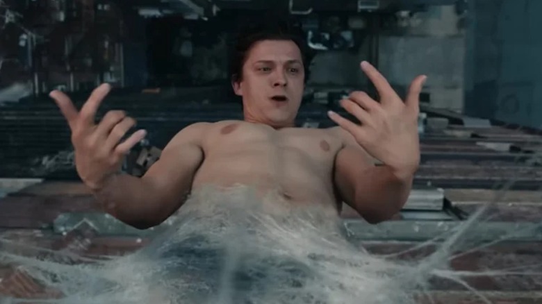Shirtless Peter Parker hanging by webbing from side of building