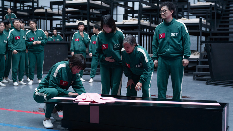 Players surrounding a gift-wrapped coffin on Squid Game