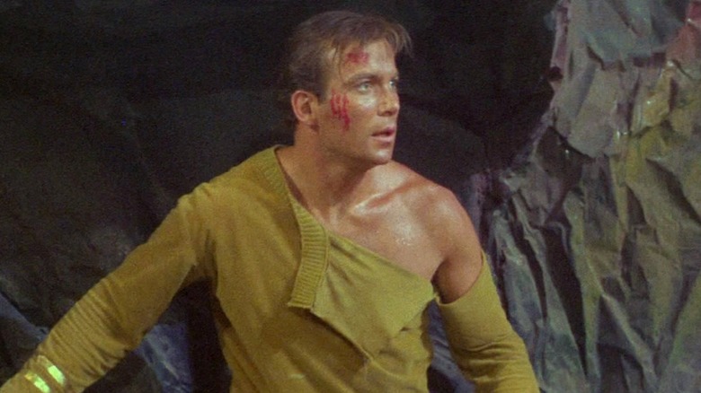 An injured Captain Kirk with his shirt torn in an episode of "Star Trek" (1966-1969)