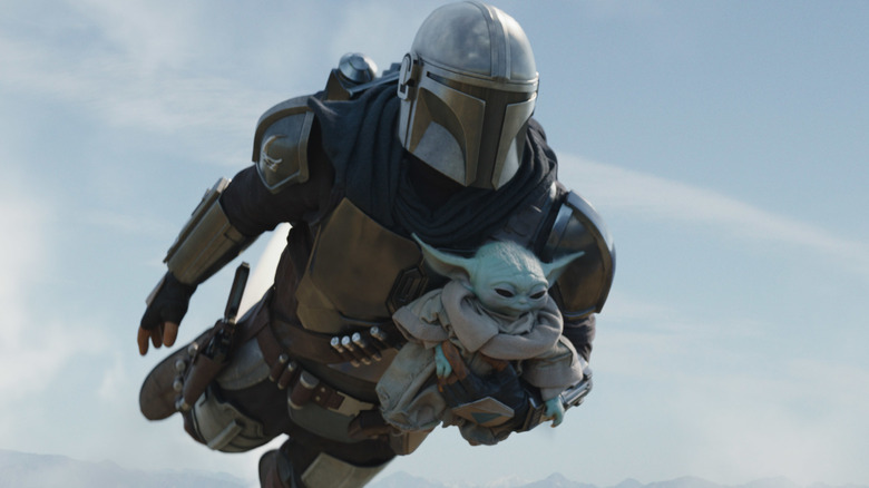 Din Djarin flying with his jetpack, holding Grogu, in "The Mandalorian" Season 2 (2020)