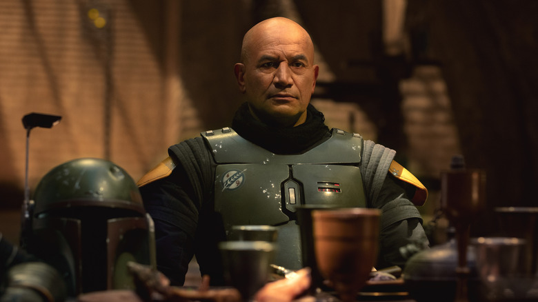 Boba Fett sitting at a table, armor on but helmet off, in The Book of Boba Fett (2021)