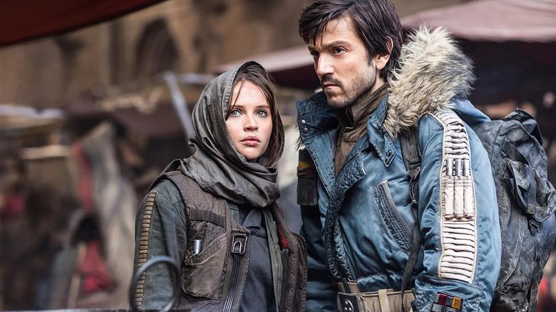 Jyn Erso wearing a dark hood, and Cassian Andor, wearing a blue parka, stand in a desert bazaar in "Rogue One"