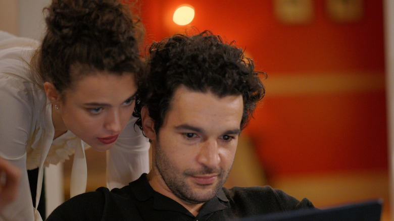 Rebecca looking over Hal's shoulder as he uses laptop in Sanctuary (2022)