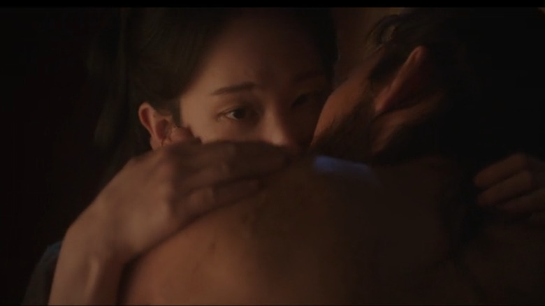 Woo being kissed by a man as she rubs his shoulder in Queen Woo (2024)