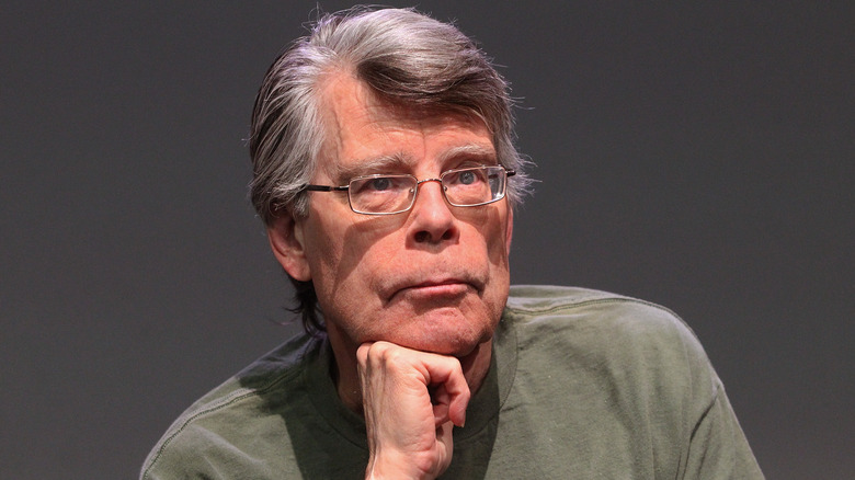 Stephen King posing against a gray background with his head resting on his fist