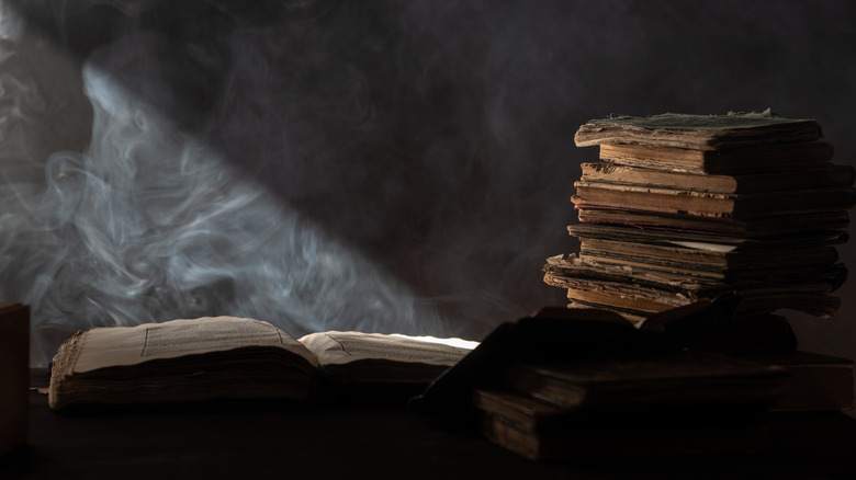 An open book with fog above it and a pile of ominous books beside it