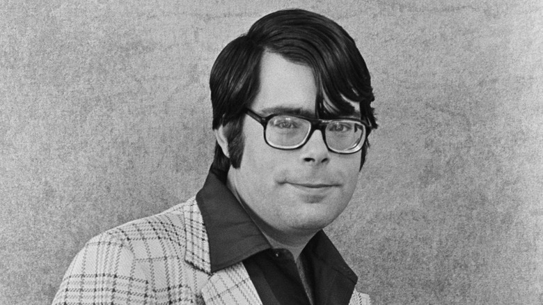 Stephen King with his hair parted, in a shirt with a big collar and dark-rimmed glasses