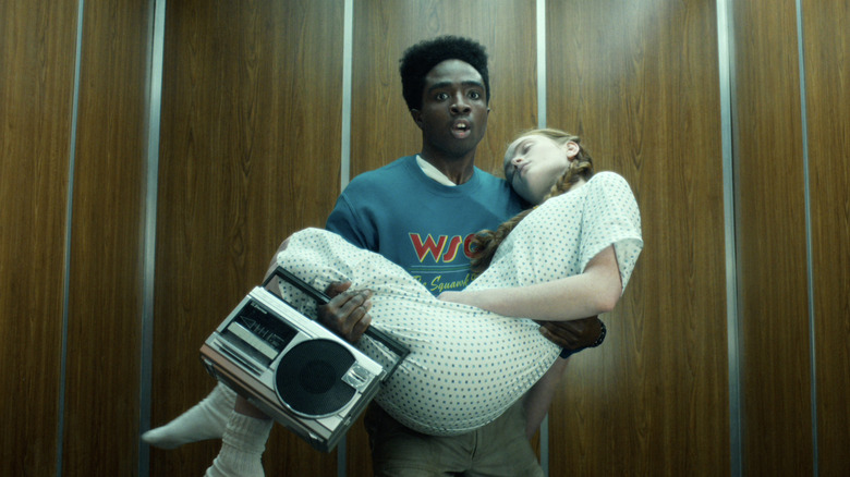 Lucas carrying a comatose Max in an elevator while holding a boombox in Stranger Things 5