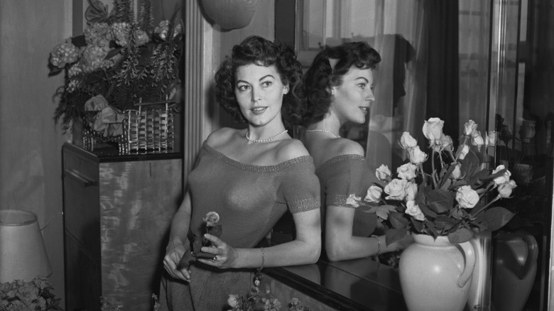 Ava Gardner standing with her back to a mirror and holding a flower