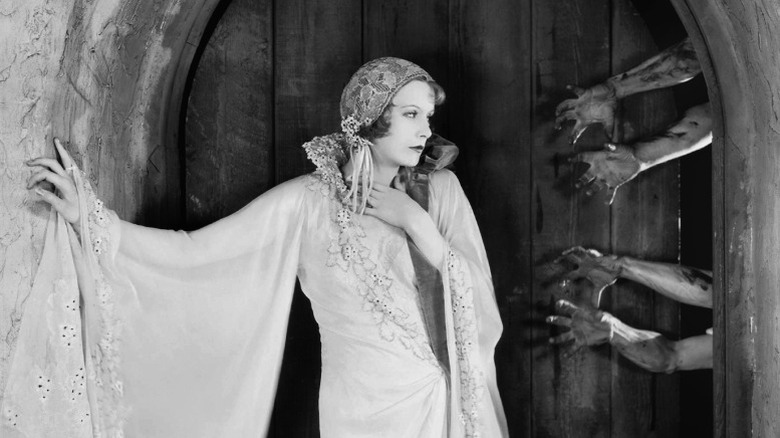 Greta Garbo looking at maimed hands reaching out towards her from behind a door