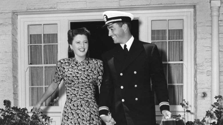 Barbara Stanwyck and Robert Taylor walking out into a front yard and holding hands