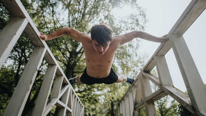Shirtless man balancing between two metal fences