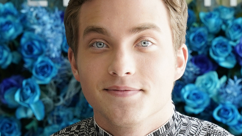 Jordan Elsass smiling against a wall of blue flowers