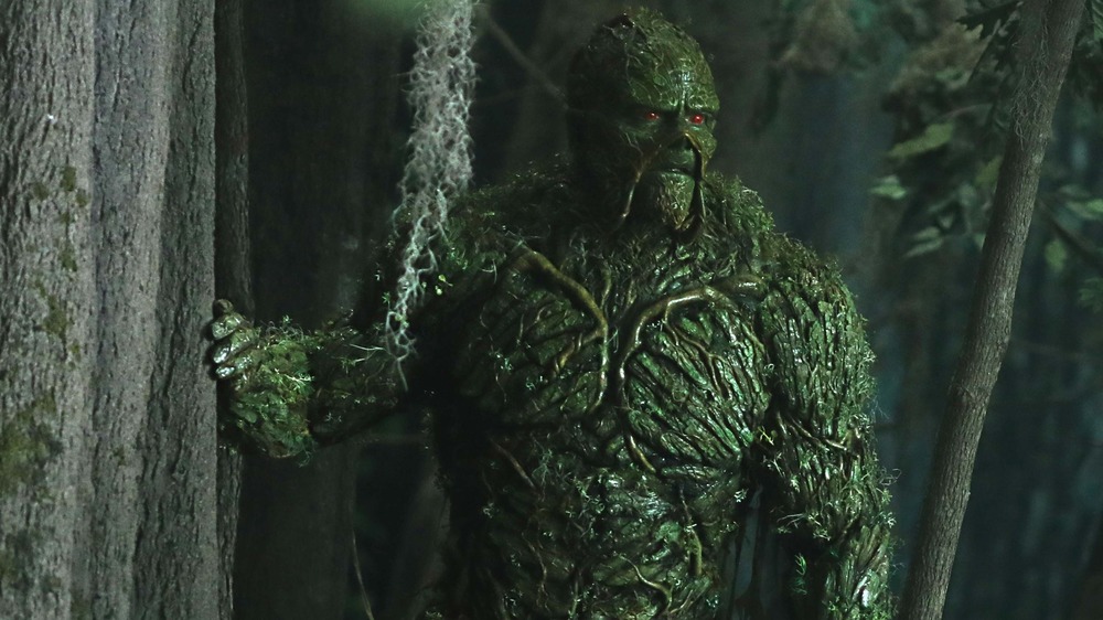 Swamp Thing peers off into the distance while touching a tree