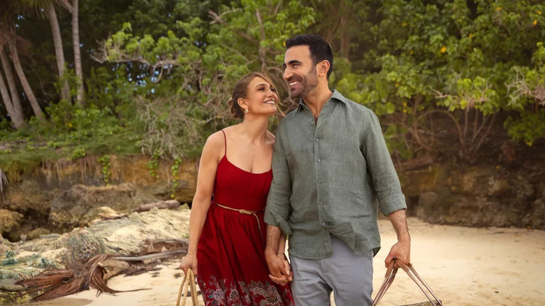 Jackie and Daniel holding hands on a beach together in Office Romance
