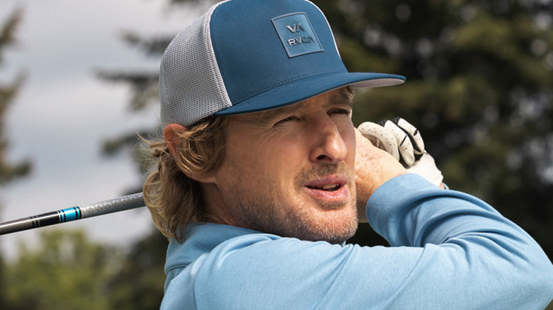Pryce Cahill finishes a drive in a blue hat and shirt in 