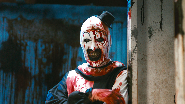 Art the Clown smiles with arms folded, splattered with blood