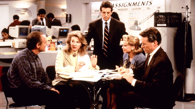 The news team gathered together around a table in "Murphy Brown"