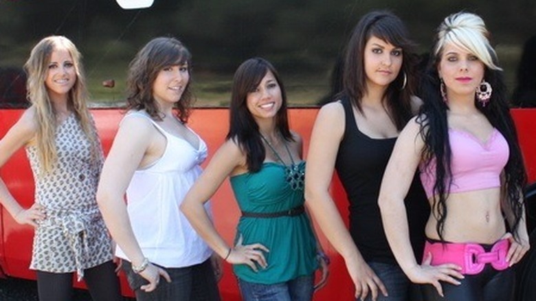 Female contestants standing in front of the "Next" bus