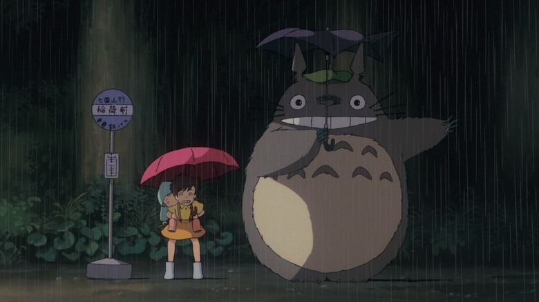 Mei, Satsuki, and Totoro wait at a bus stop in the rain in "My Neighbor Totoro" (1988)