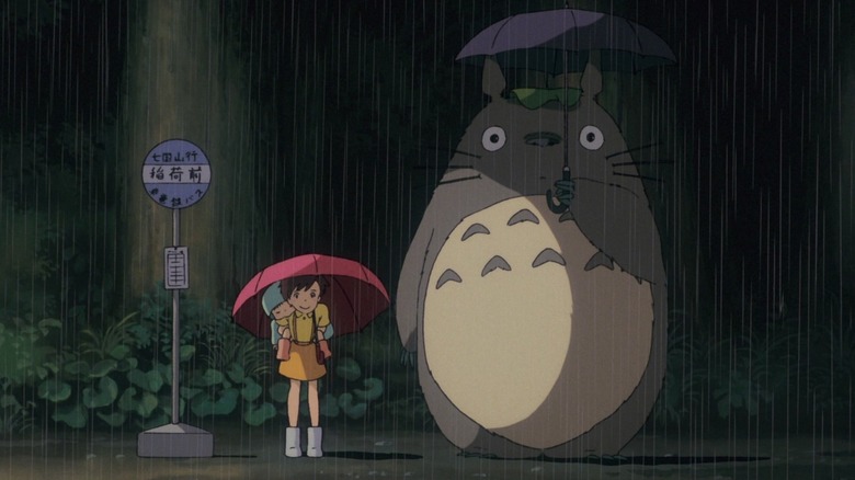 Satsuki, Mei, and Totoro standing at a bus stop in "My Neighbor Totoro" (1988)