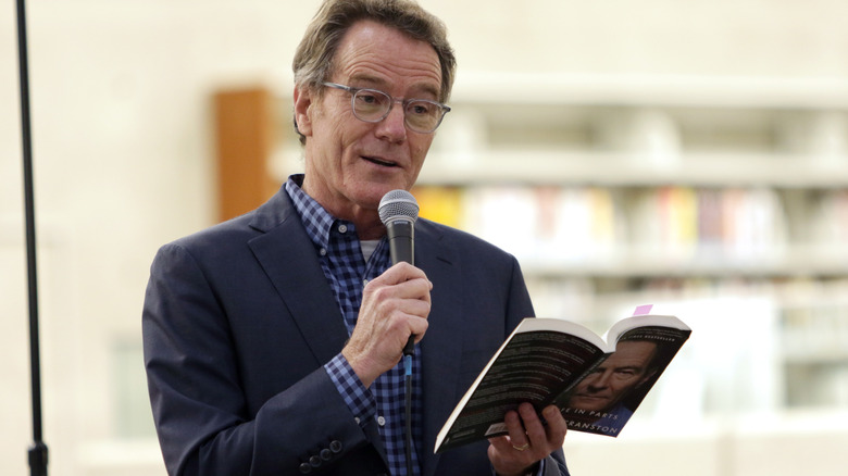 Bryan Cranston holding a microphone and a book
