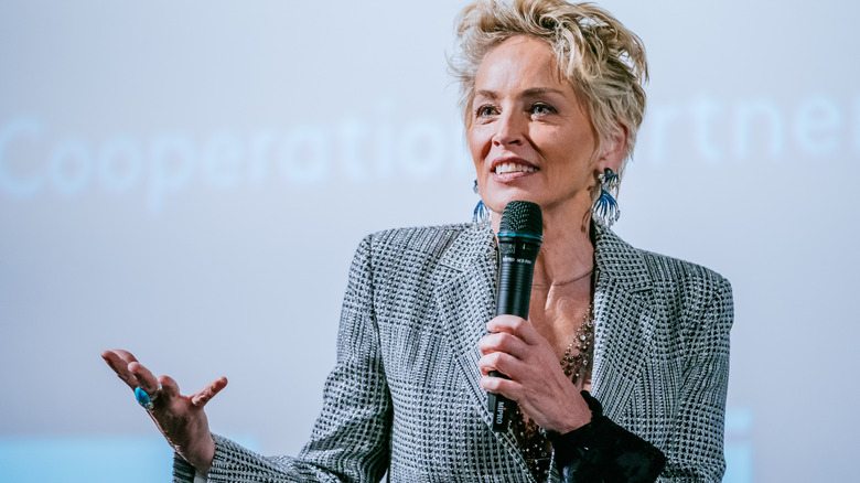 Sharon Stone in a grey suit holding a microphone