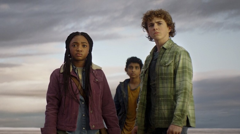 Annabeth (Leah Sava Jeffries), Grover (Aryan Simhadri), and Percy (Walker Scobell) staring down Ares (Adam Copeland) on a beach