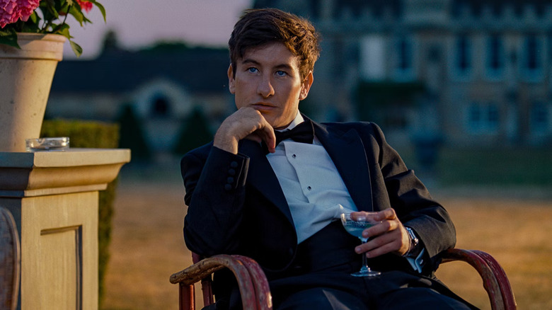 Oliver sitting in a chair holding a drink in Saltburn