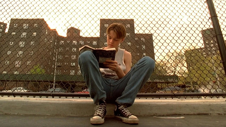 Jim (Leonardo DiCaprio) sits in front of a chain link fence writing in a diary in the Basketball Diaries