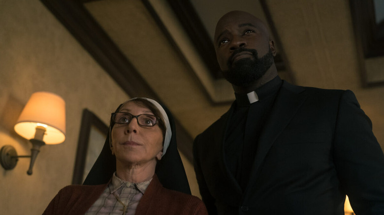 Acosta walks down a hall accompanied by a nun in "Evil" (2019-2024)