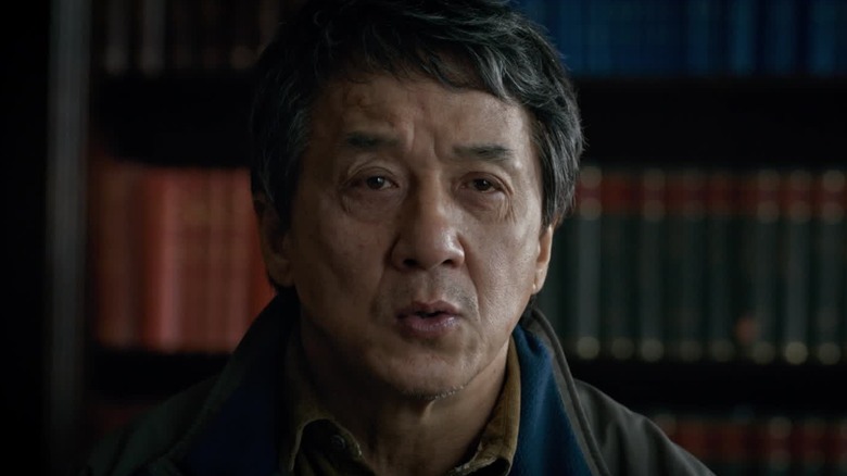 Quan sitting in front of a shelf of books in The Foreigner