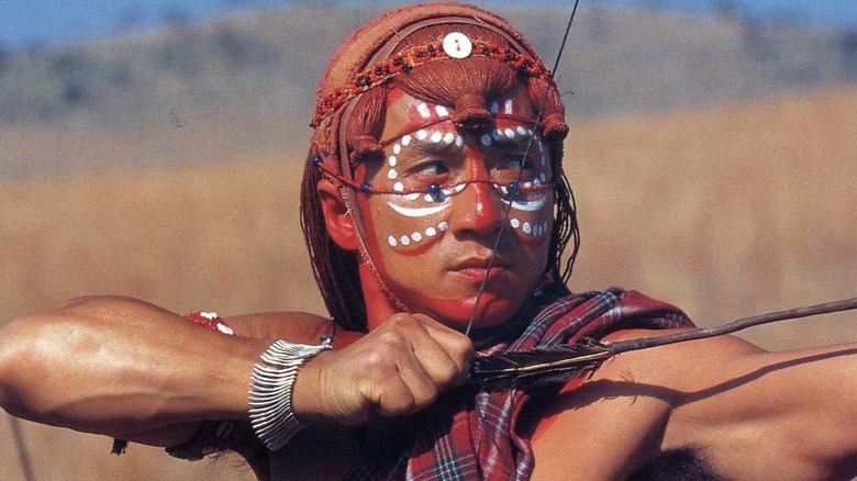 Jackie Chan wearing tribal attire and aiming an arrow in Who Am I?