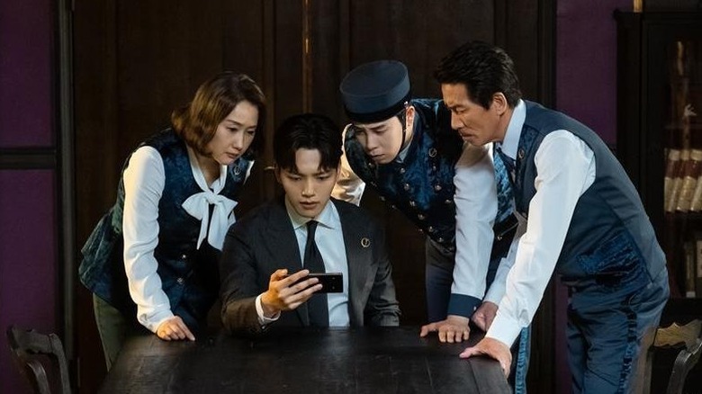 People gather around to look at a phone in Hotel del Luna (2019)