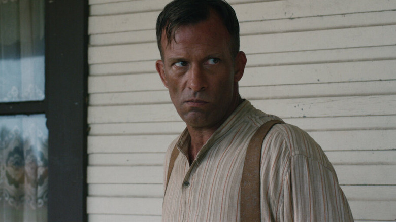Wilfred stands on the porch with a sinister look on his face in 1922.