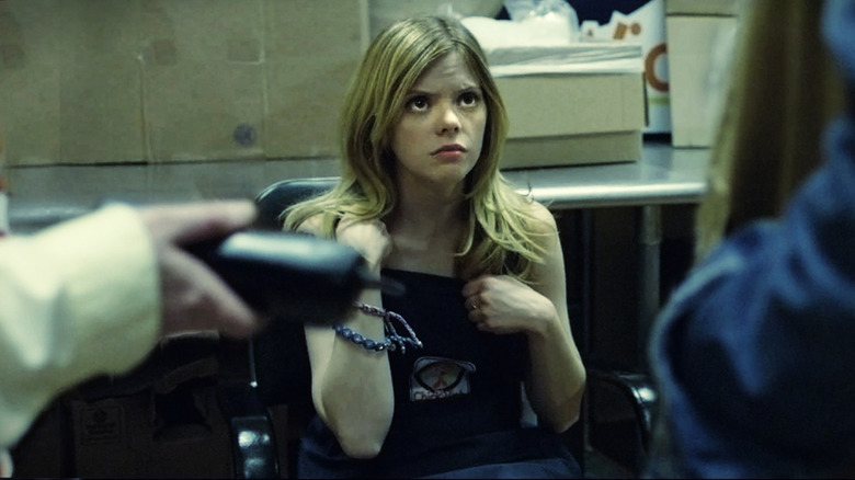 Becky sits in a chair looking worried in Compliance.