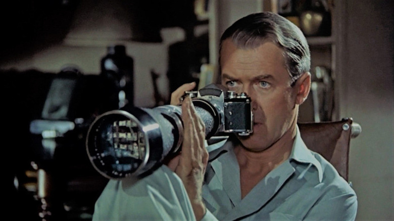 Jeff holds a large camera and peers through a window in Rear Window.