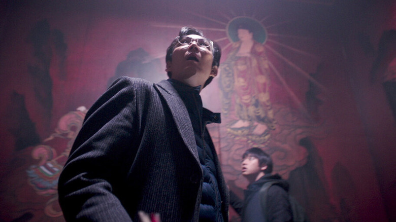 Park looks around a dark chamber with strange art on the walls in Svaha: The Sixth Finger.
