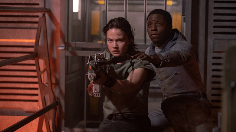 Rain holding a gun while Andy stands behind her