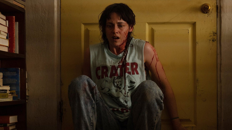A bloodied Lou crouches behind her door in "Love Lies Bleeding"