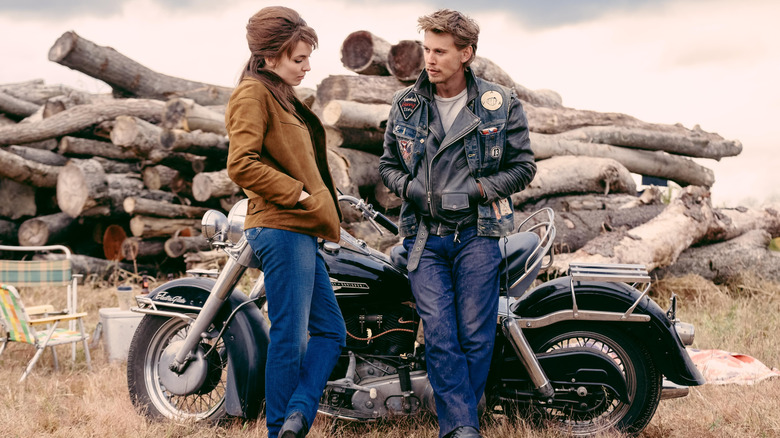 Kathy and Benny stand near a motorcycle in "The Bikeriders"