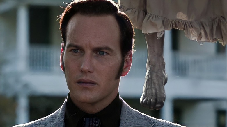 Ed stands in the yard with a dead body dangling behind him in "The Conjuring" (2013)