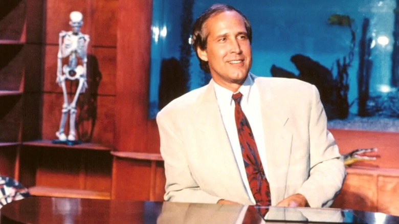 Chevy Chase sitting at his desk on "The Chevy Chase Show"