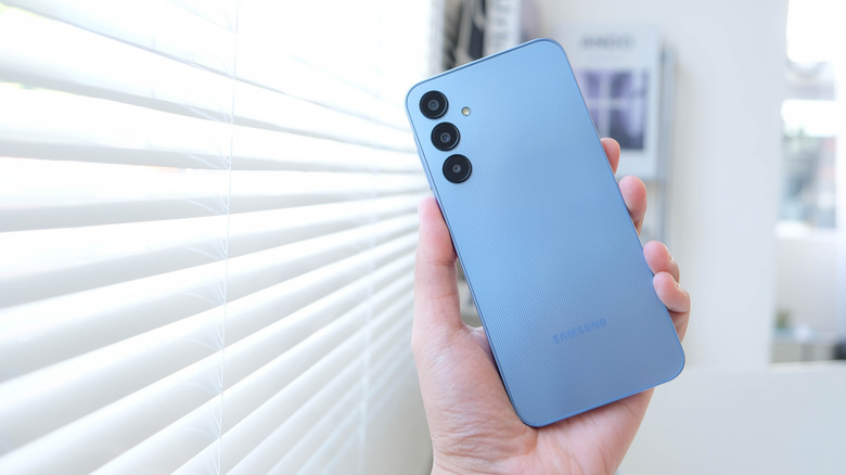 The back of a blue Samsung Galaxy A25 phone being held in a person's left hand.